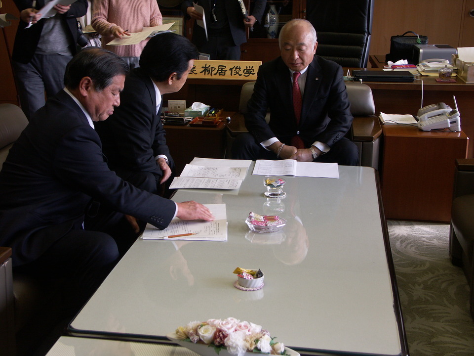 柳居議長（右）に説明する新藤会長（中央）、小泉副会長（左）の画像