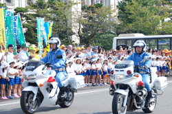 山本知事や幼稚園児らに見送られて出発する車両隊