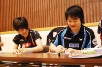 岸川選手と共にうちわにサインをする石川さんの画像