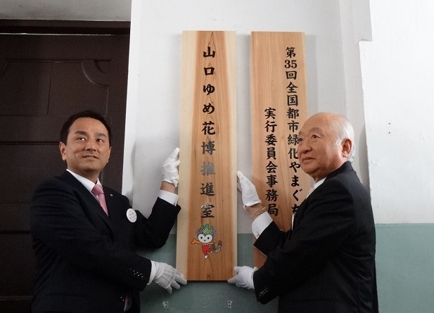 山口ゆめ花博推進室前で看板掲出をする柳居議長と村岡知事