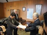 柳居議長（右）に答申する新藤会長（左）、西嶋副会長（左奥）の画像