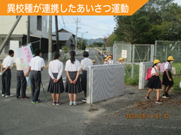 中学生が小学校正門であいさつをしているようすです。